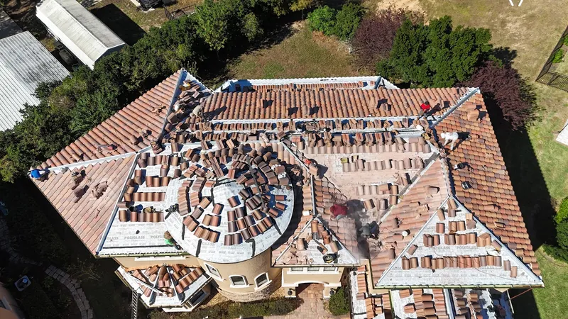 Aerial view of a Florida Gulf Roofing crew installing a clay barrel-tile roof, with tiles staged across the underlayment and workers spread over the roof deck