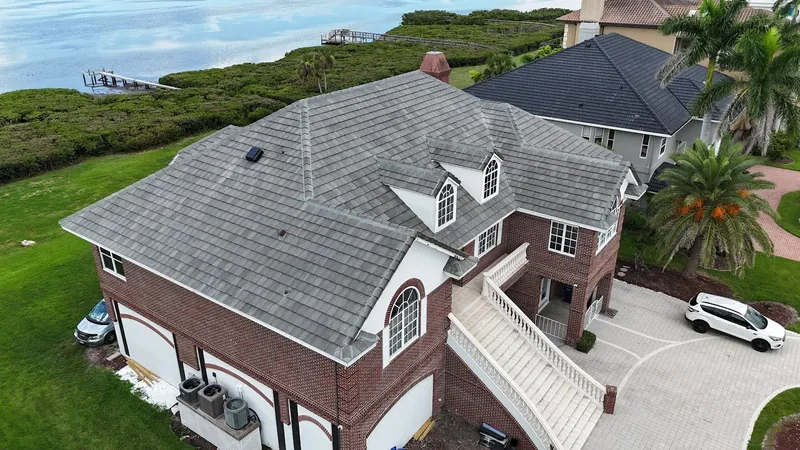 Aerial view of a completed gray flat-tile roof on a waterfront brick home on Florida's Gulf Coast, with a private dock and bay beyond
